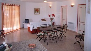 Ein Essbereich mit Tisch und Stühlen, ein Bett mit rotem Kopfteil, ein Fernseher und ein Bild an der Wand.