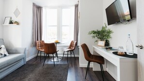 A modern living room with a grey sofa, two brown leather chairs, a glass coffee table, and a TV mounted on the wall. - Design Suites Lytham (Lytham St. Anne's)