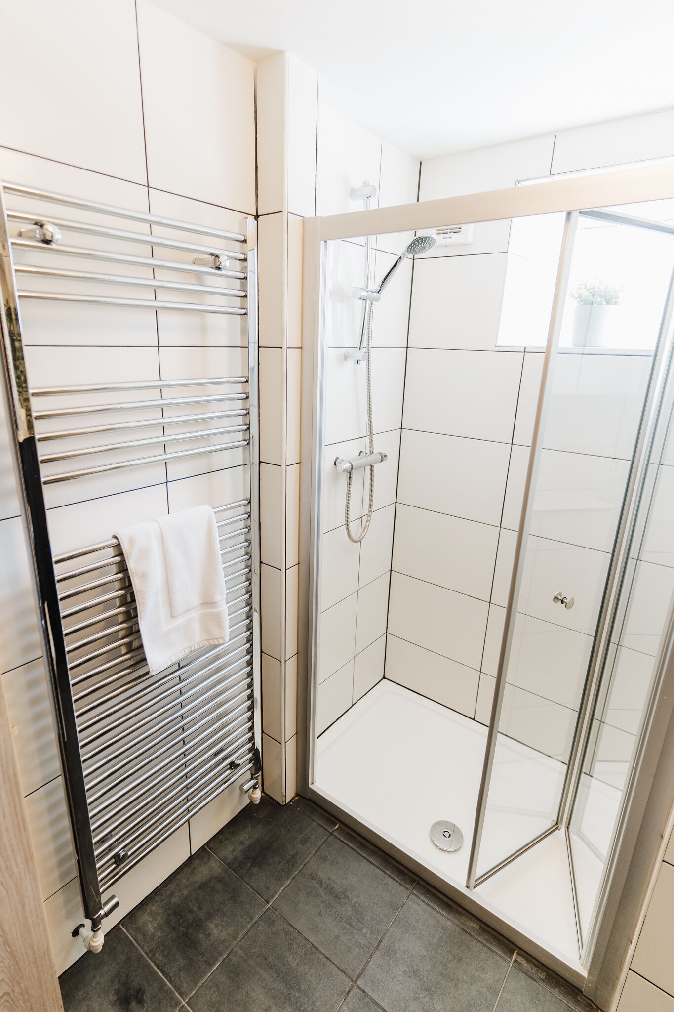 A modern bathroom with a glass-enclosed shower, a towel rack, and a tiled floor.