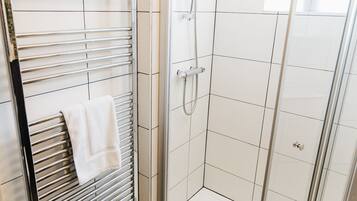 A modern bathroom with a glass-enclosed shower, a towel rack, and a tiled floor.