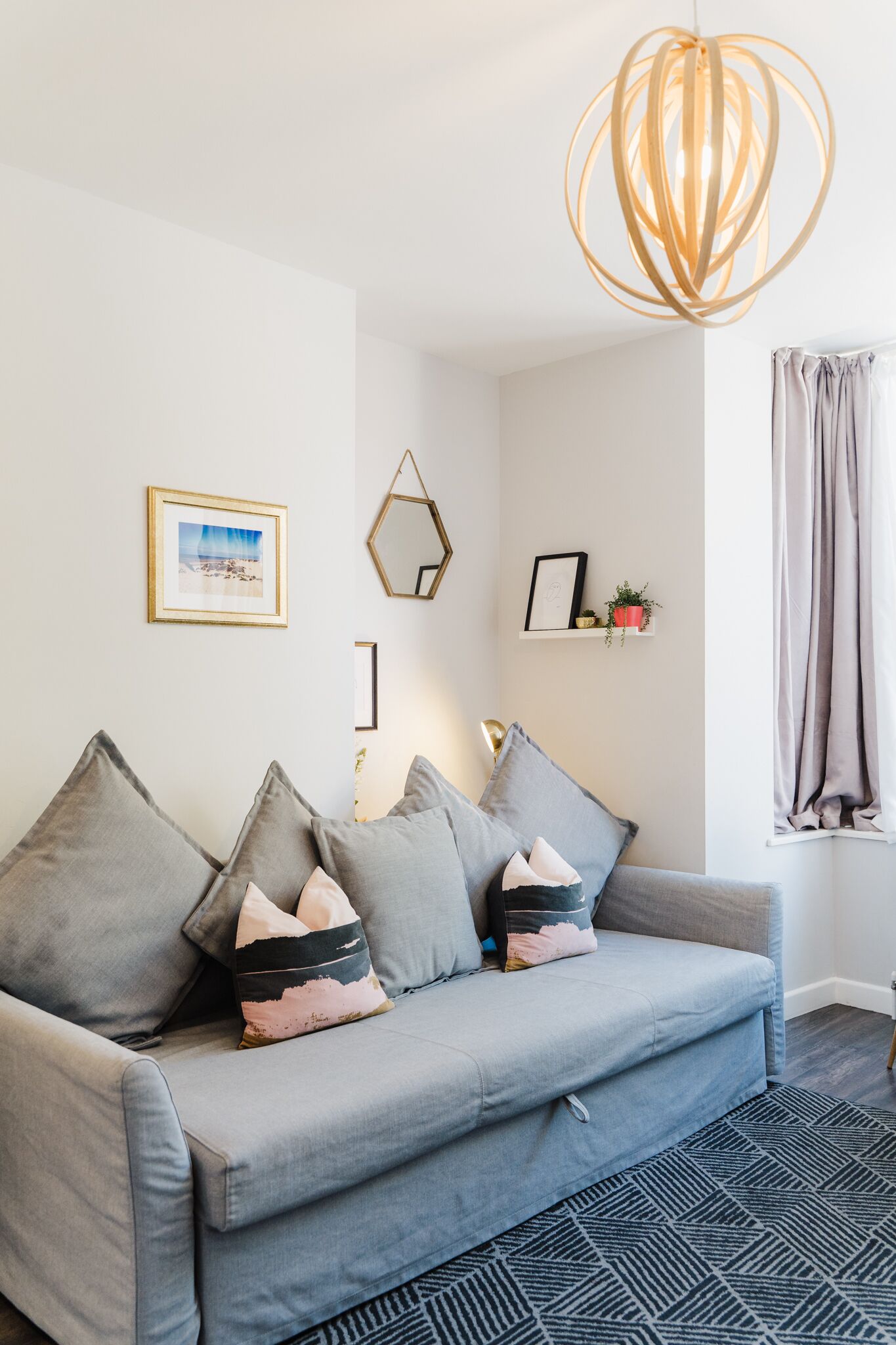 Un salon moderne avec un canapé gris, des coussins décoratifs, une suspension au design géométrique et un tableau encadré accroché au mur.