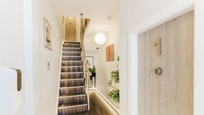A modern interior with a wooden staircase, a door with a keypad, and a wall-mounted plant. - Design Suites Lytham (Lytham St. Anne's)