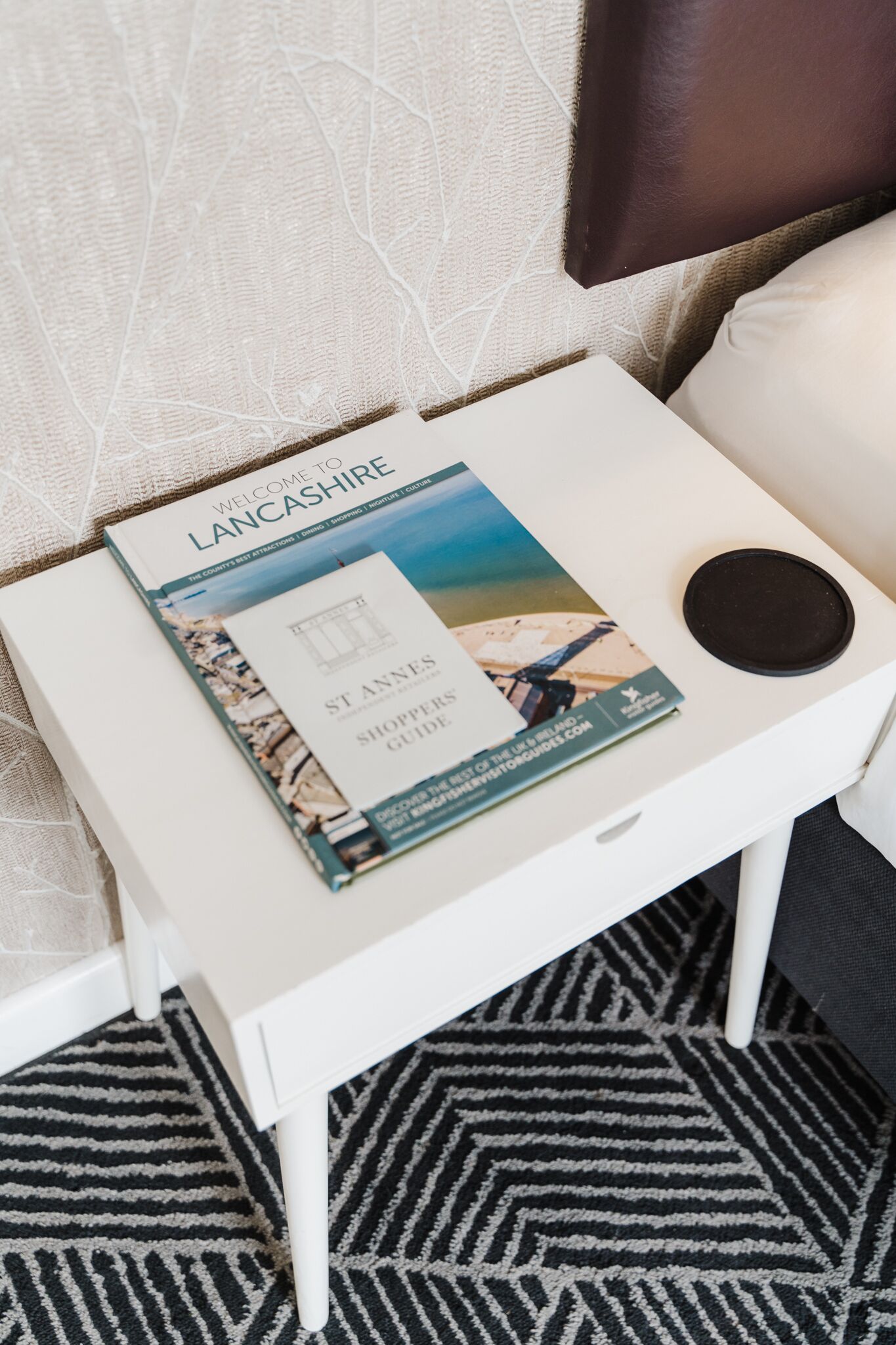 A white bedside table with a book titled "Welcome to Lancashire" and a "St Annes Shoppers Guide" on it.