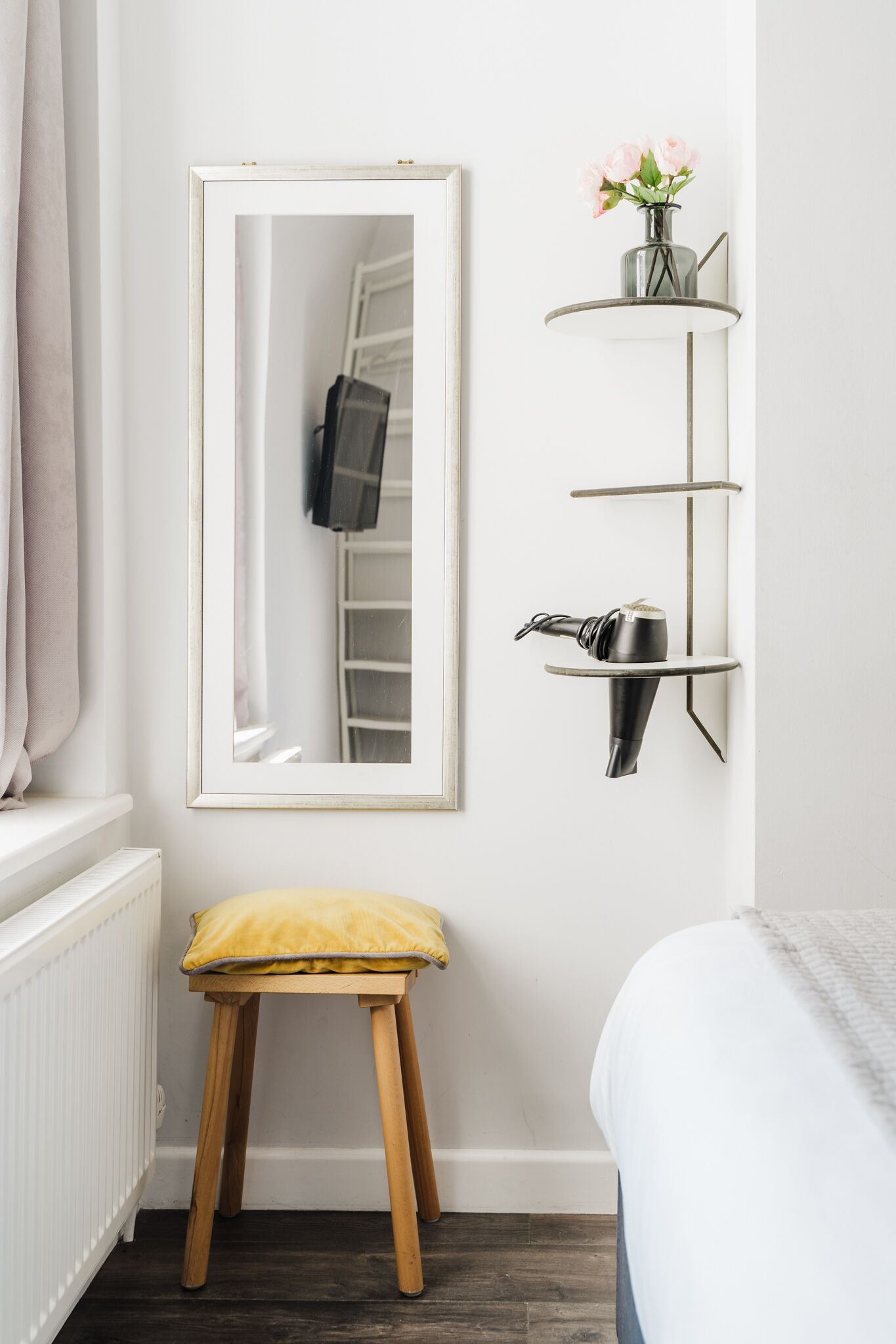 Een kamer met een grote spiegel, een klein krukje, een plank met een vaas en een radiator.