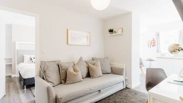 A modern living room with a sofa, a dining table, and a kitchen area in the background.
