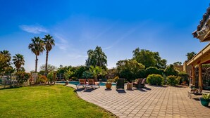 A paved patio area with outdoor furniture, a swimming pool, and palm trees. - Ranch Home with Guest Suite Located on 2 acres of Orchard (Waddell)