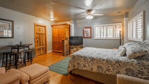 A bedroom with a bed, a television, a wooden cabinet, a desk with stools, and a ceiling fan. - Ranch Home with Guest Suite Located on 2 acres of Orchard (Waddell)