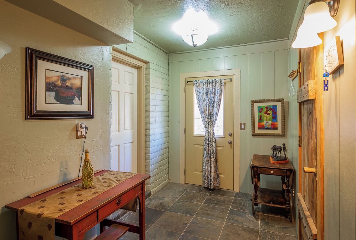Un couloir avec un banc en bois, une porte ornée d’un rideau à motifs et une petite table sur laquelle est posé un objet décoratif.