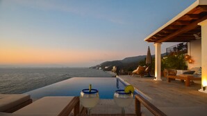 A poolside view with two glasses of a light-colored drink, a wicker chair, and a lounge area overlooking the sea. - Private villa- 3 bdrm & 4 bath with ocean views and new private infinity pool  (Puerto Vallarta)