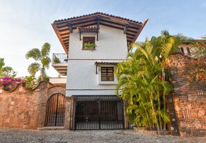 A two-story building with a white facade, a tiled roof, and a stone wall.