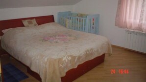 Ein Schlafzimmer mit einem Einzelbett, einem Babybett, einem Fenster mit Vorhängen und einer Heizung.