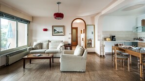 A spacious living room with a sofa, armchair, and coffee table. A kitchen is visible in the background with a dining area. - Residence Schuler - Apartment 'B' with sea-Etna view  (Taormina)