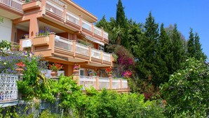 A multi-story building with balconies, surrounded by lush greenery and flowering plants. - Residence Schuler - Apartment 'B' with sea-Etna view  (Taormina)