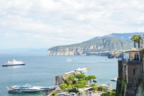 Un pueblo costero con una torre destacada, barcos y un acantilado rocoso.