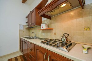 Una cocina con armarios de madera, estufa a gas, pileta y salpicadero con azulejos.