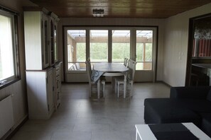 A spacious kitchen with a dining table and chairs, large windows, and a black sofa.