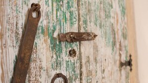 Eine rustikale Holztür mit abblätternder Farbe und Metallbeschlägen, darunter ein Riegel und ein Ring.