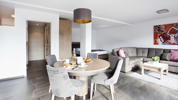 Una sala de estar moderna con una mesa redonda de comedor, sillas tapizadas en gris, un sofá gris y una mesa de centro.