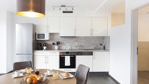 Una cocina moderna con armarios blancos, microondas, cafetera y comedor con mesa dispuesta para el desayuno.