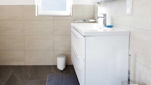 Un baño moderno con tocador blanco, un espejo grande y una ventana.