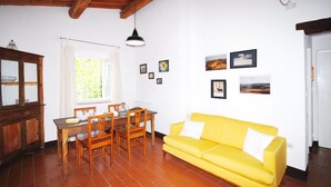 A living room with a yellow sofa, wooden dining table, chairs, and a window with curtains.