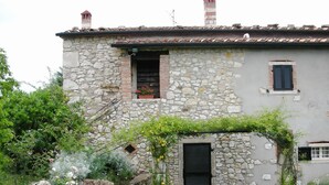 A stone building with a small window and a door, surrounded by greenery and flowers.