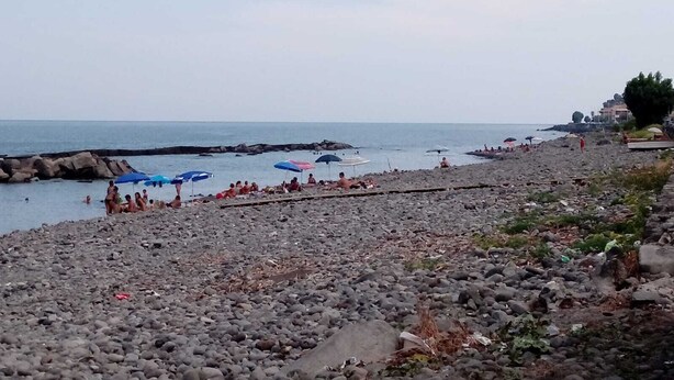 Ein felsiger Strand mit Sonnenschirmen und Menschen.