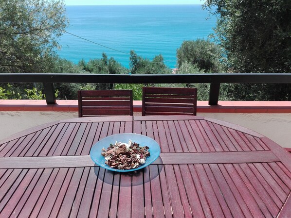 A wooden deck with a table and two chairs facing a scenic view of the ocean.