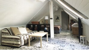 A cozy attic room with a sloped ceiling, a sofa, a small table, and a lamp. - Large bedroom above an artist's studio (Triguères)