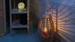 En trähylla med ljus, en blå handduk, ett sfäriskt föremål och en flätad lykta mot en trävägg.