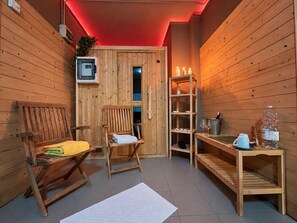 A sauna room with wooden walls, a bench, a chair, a shelf with candles, and a water bottle. - Il Perugino | Agriturismo with covered patio (Paciano, PG)