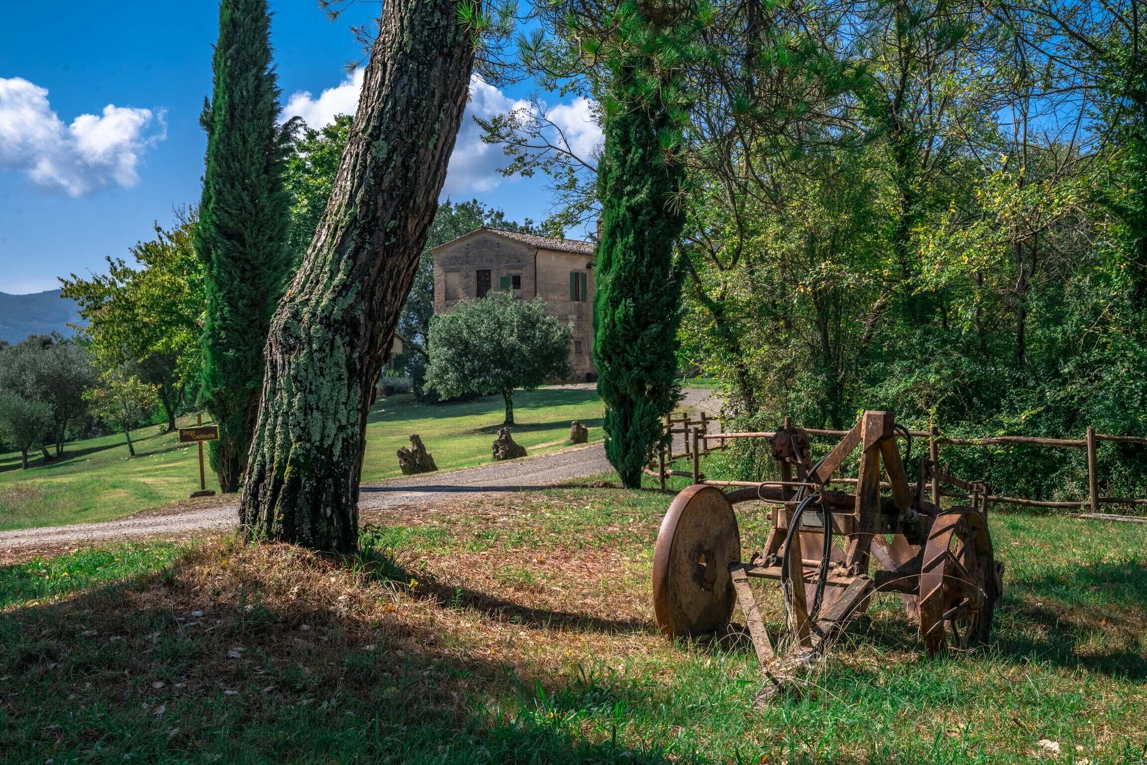 A rustic farm scene with a large tree, a wooden fence, and a vintage tractor.