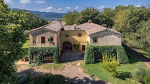 A two-story stone house with a tiled roof, surrounded by lush greenery and a gravel driveway. - The Real Tuscany great for families and friends. (Buonconvento, Siena)