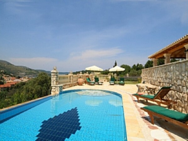A swimming pool with lounge chairs and umbrellas, surrounded by stone walls and a view of the countryside. - Villa Loukas (3 Bedroom, Sleeps 6) (Anatoliko)