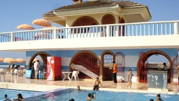 A swimming pool area with multiple people in the water, a lifeguard stand, and a covered seating area with umbrellas. - Sea view, large swimming pool, penthouse in luxury residence (Unknown)