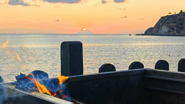 A sunset over a body of water with a fire burning in the foreground.