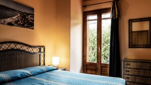 A bedroom with a bed, a nightstand, a dresser, a window with curtains, and a wall-mounted mirror.