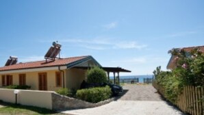A house with a solar panel on the roof, a covered porch, and a gravel driveway leading to the entrance.