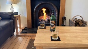 Un salon chaleureux avec une cheminée, une table en bois sur laquelle se trouvent une bouteille de bière et un verre, et un canapé en cuir.