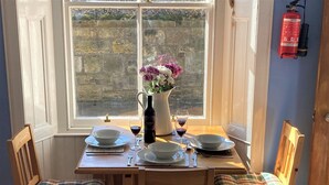Une table à manger dressée avec des assiettes, des verres et une bouteille de vin, et un vase rempli de fleurs placé au centre.