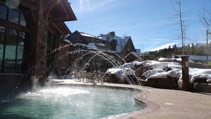 A pool with water features, a stone facade building, and a clear blue sky. - Grand Lodge @ Peak 7, Spring Break, Mar 21-28 2026 only, 2 BR condo - sleeps 8 (Breckenridge)