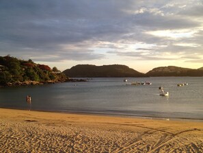 A beach with a sandy shore, calm water, and boats.