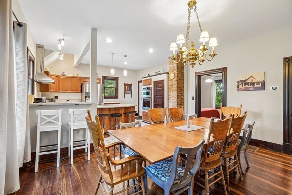 A spacious dining area with a wooden table and chairs, a chandelier, and a kitchen in the background. - Historic charm in downtown Tryon; 18 Minutes from Tryon Intl Equestrian Center (Tryon)