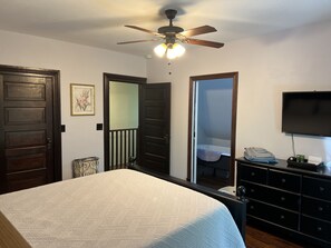 Une chambre à coucher comprenant un lit, une commode, un miroir, un ventilateur de plafond et un téléviseur.