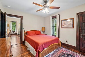A bedroom with a wooden bed, a ceiling fan, a window with curtains, and a door. - Historic charm in downtown Tryon; 18 Minutes from Tryon Intl Equestrian Center (Tryon)