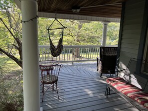 Une véranda abritée avec une table et des chaises, un hamac suspendu et un banc doté d’un coussin à rayures.
