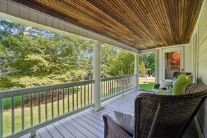 A covered porch with white railings, wicker furniture, and a view of a backyard with trees and a patio area. - Historic charm in downtown Tryon; 18 Minutes from Tryon Intl Equestrian Center (Tryon)