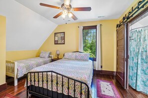 Un dormitorio con dos camas, un ventilador de techo, una ventana con cortinas y una puerta con cortinaje.