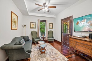 A living room with a ceiling fan, a television, a wooden cabinet, and a view of the outdoors through a door. - Historic charm in downtown Tryon; 18 Minutes from Tryon Intl Equestrian Center (Tryon)