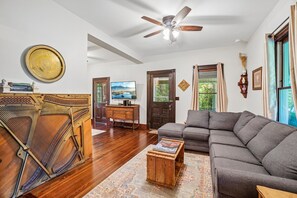 A living room with a sofa, a television, a wooden floor, and a ceiling fan. - Historic charm in downtown Tryon; 18 Minutes from Tryon Intl Equestrian Center (Tryon)